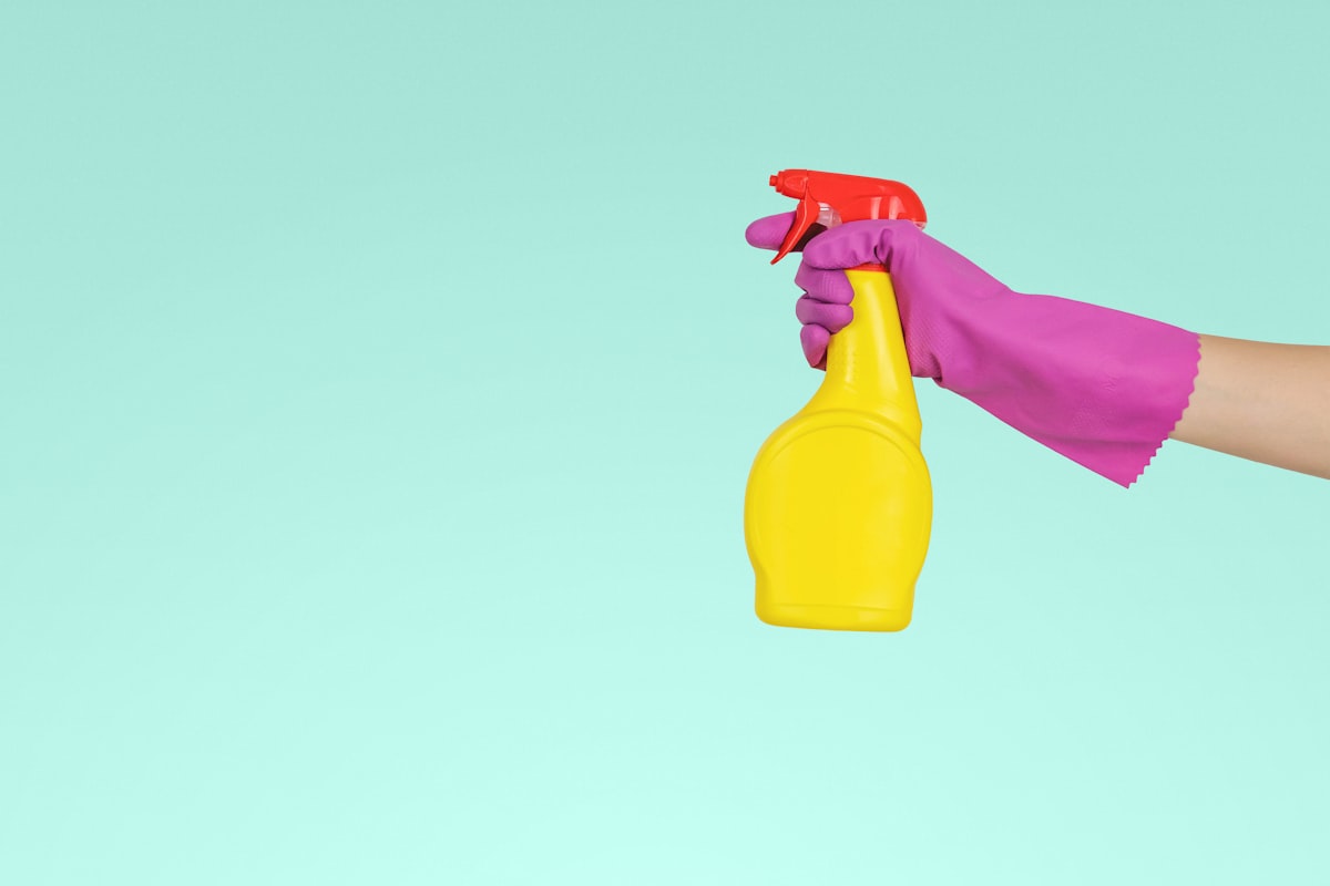 Hand mit Reinigungsspray vor türkisem Hintergrund